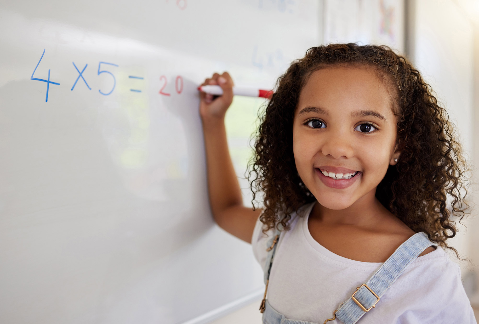 little girl writing a math problem on whiteboard and smiling