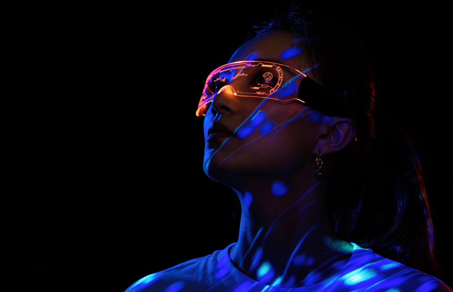 portrait image of a woman in the dark wearing transparent VR goggles with information displaying on the lenses in neon orange